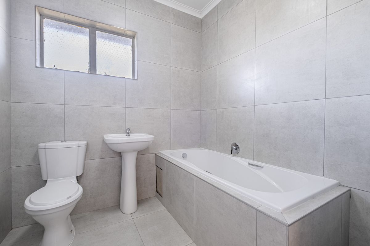 A clean, modern bathroom featuring neutral wall and floor tiles, a pedestal basin, a toilet, and a built-in bathtub.