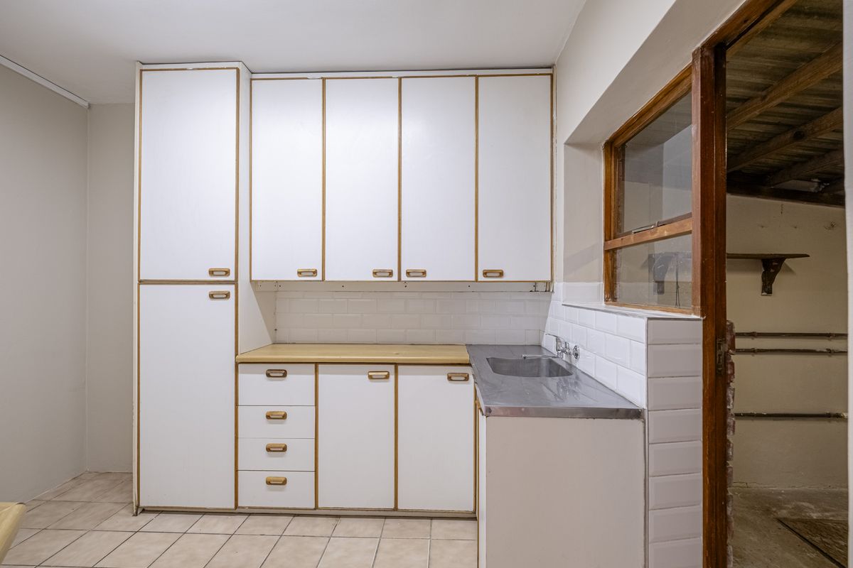 A compact kitchen featuring white cabinetry, a stainless steel sink, subway tile backsplash, and ceramic floor tiles, offering a functional space ready for modernization.