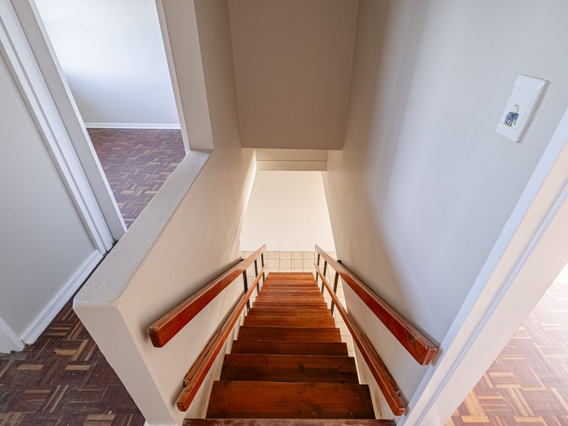 A view looking down a wooden staircase featuring parquet flooring in the surrounding hallway areas.