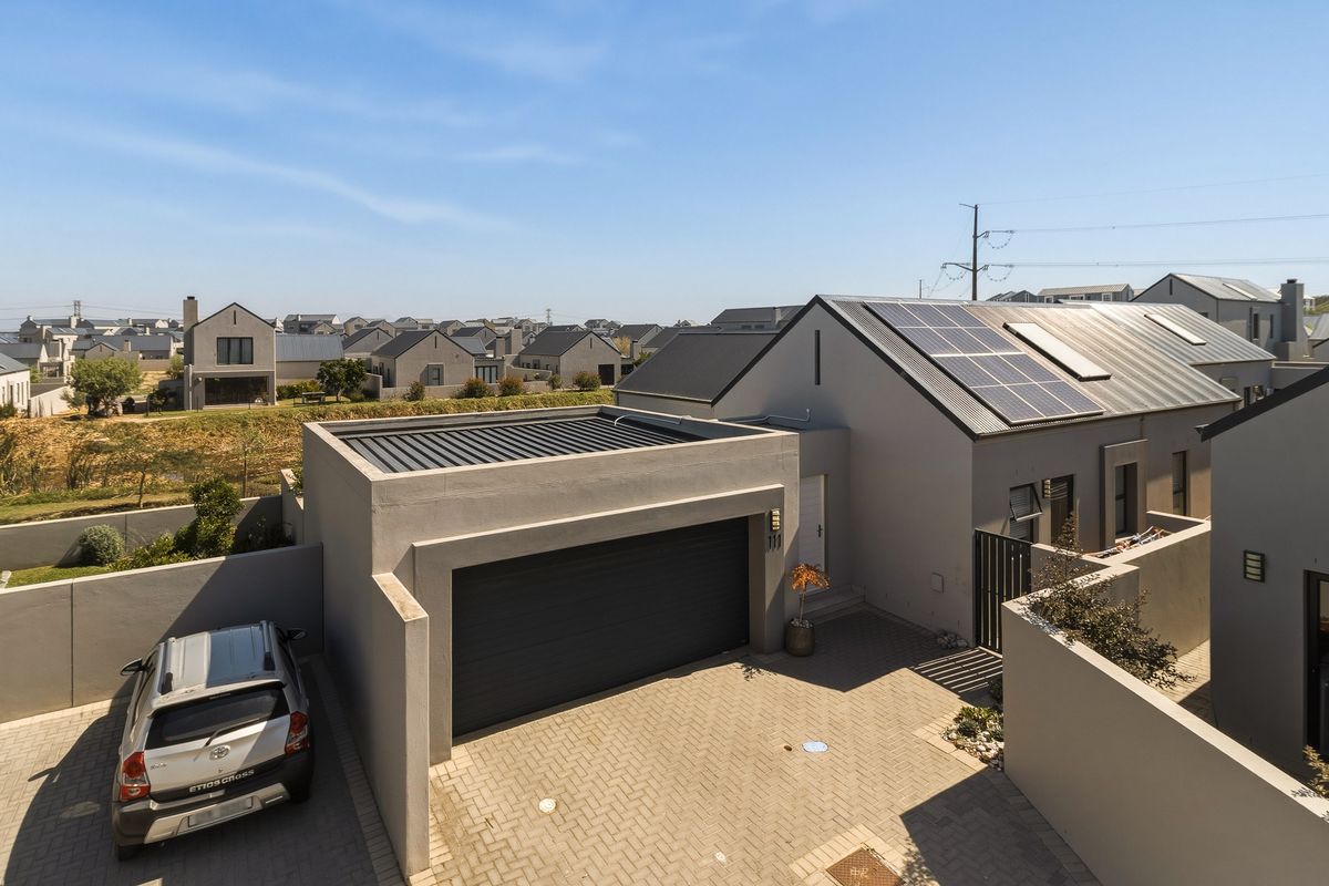Aerial view of a modern residential property featuring a paved driveway, garage, and solar panels installed on the metal roof.