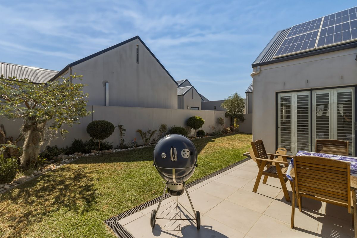 A well-maintained rear garden featuring a tiled patio area, boundary wall, and solar panels installed on the roof.