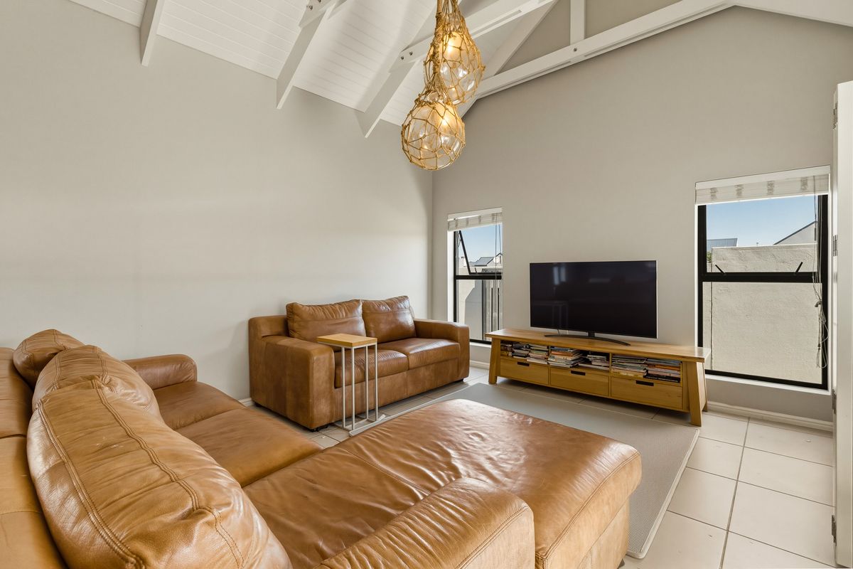 Spacious living room featuring a high vaulted ceiling with exposed rafters, tiled flooring, and large windows providing ample natural light.