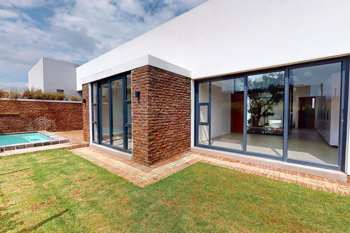 Modern rear exterior featuring a swimming pool, manicured lawn, brick boundary wall, and large sliding glass doors leading into the home.