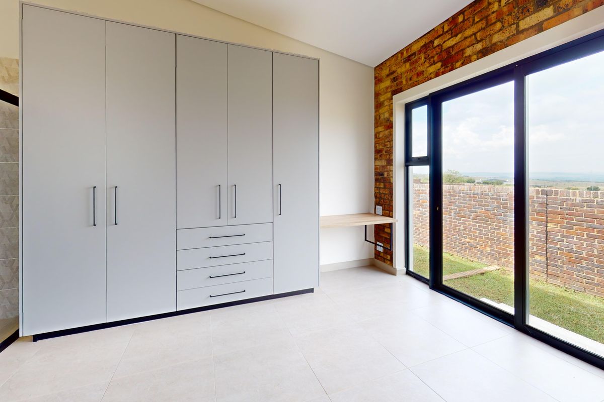 Modern bedroom featuring built-in cupboards, an exposed brick feature wall, and large sliding glass doors providing natural light and access to the exterior.