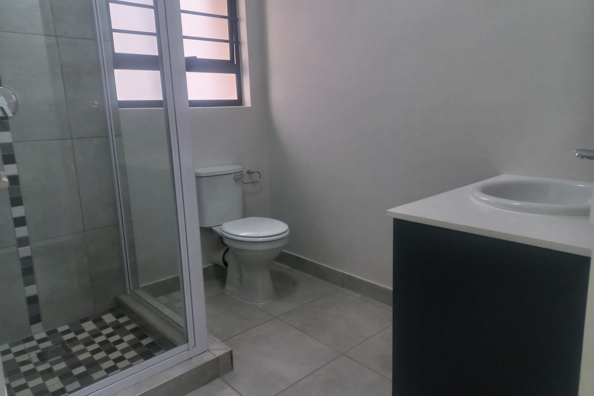 A clean, modern bathroom featuring a glass-enclosed shower, a vanity with a drop-in basin, and neutral floor tiling.