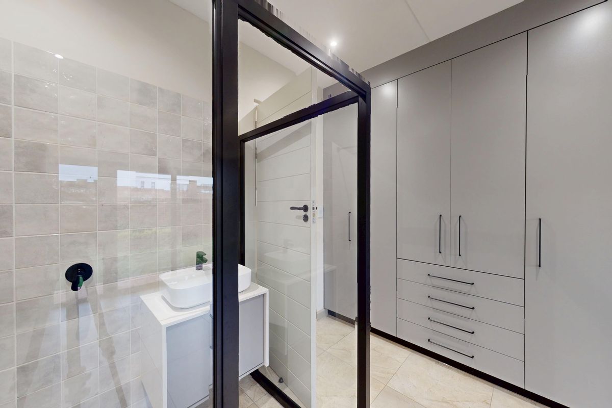 Modern bathroom featuring sleek grey built-in cabinetry, a contemporary vanity basin with black tapware, and a glass-enclosed shower area.