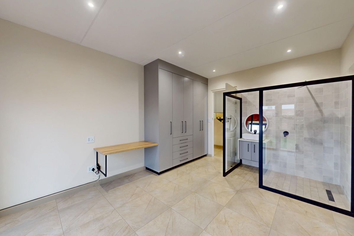Modern bedroom featuring built-in cupboards, a floating desk, and an en-suite bathroom with a glass-enclosed shower and vanity.