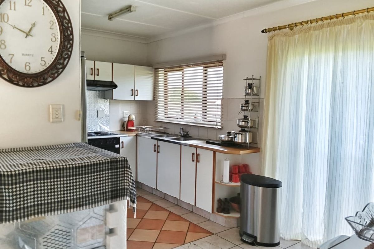 A functional kitchen featuring white cabinetry, a double sink, extractor fan, and tiled flooring with direct access to an outdoor area via sliding doors.
