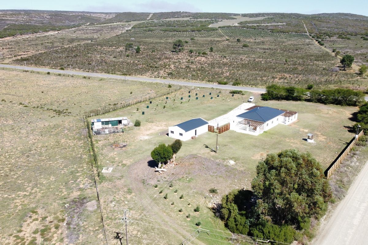 Aerial view of a farm property featuring a main dwelling with an attached patio structure, outbuildings, and expansive surrounding agricultural land.