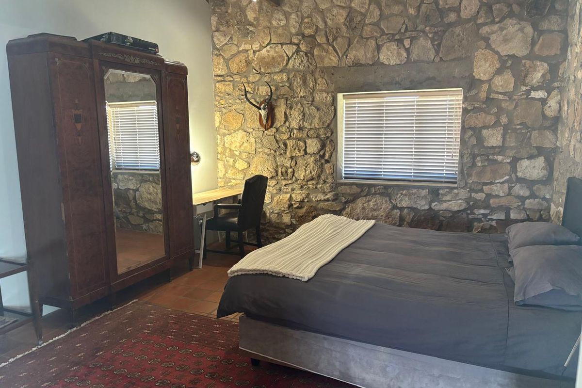 A rustic bedroom featuring exposed natural stone walls, terracotta floor tiles, and a vaulted ceiling, creating a warm and character-filled living space.