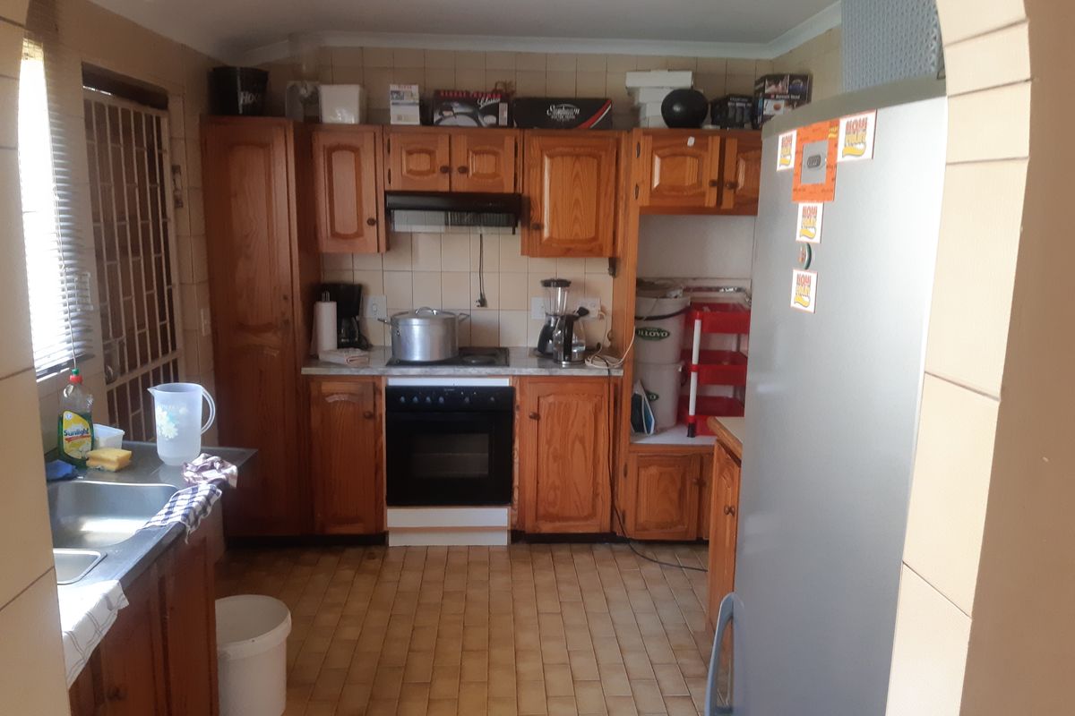 A functional kitchen featuring traditional wooden cabinetry, built-in oven, extractor fan, and tiled flooring, offering potential for a modern renovation.