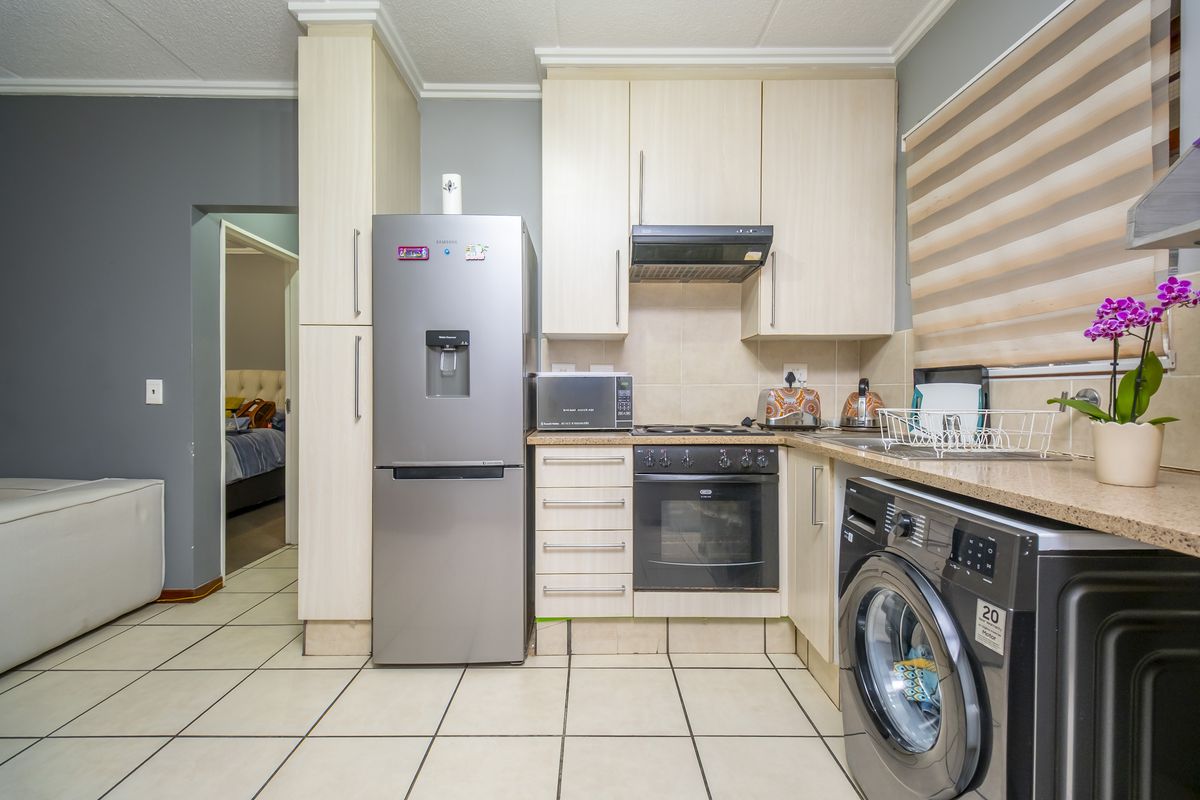 Compact kitchen featuring light wood cabinetry, built-in oven, extractor fan, and tiled flooring with direct access to the adjacent bedroom.