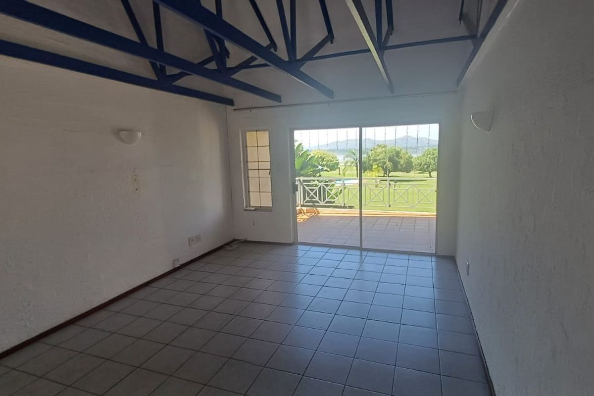An empty living room featuring exposed blue roof trusses, tiled flooring, and a sliding glass door leading to a balcony with scenic views.