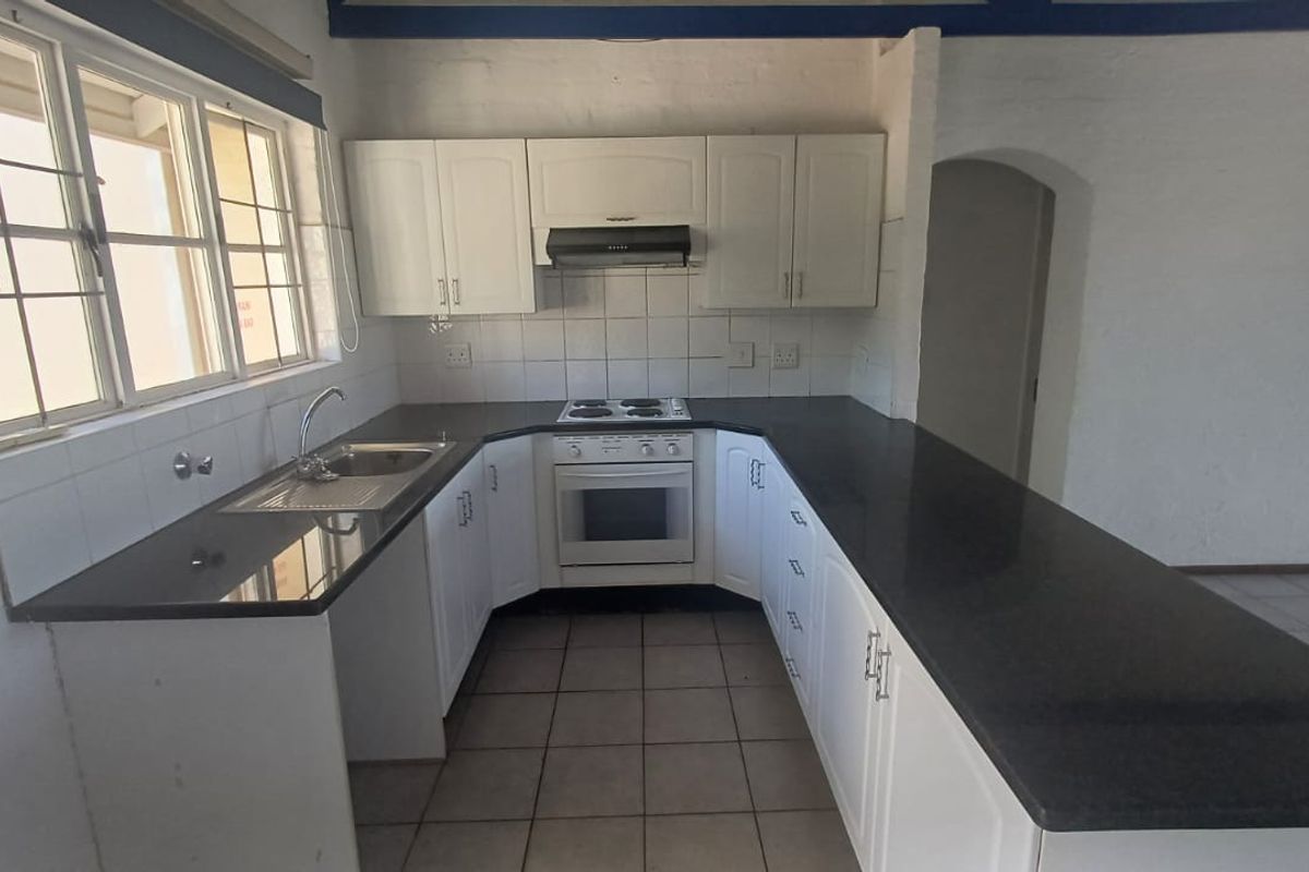 A functional kitchen featuring white cabinetry, dark countertops, an integrated electric stove and oven, and tiled flooring in an open-plan layout.