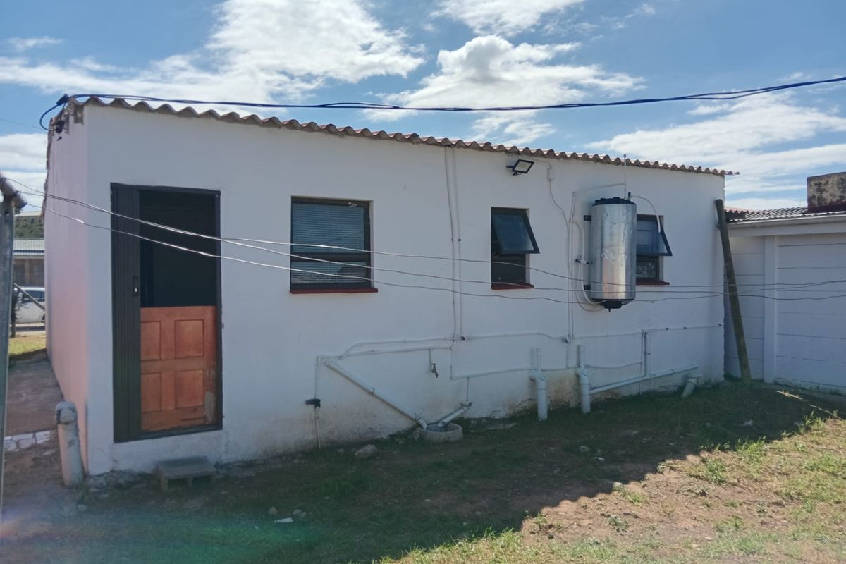 Rear exterior view of the property featuring exposed plumbing, an external geyser unit, and a security door with corrugated roof finish.
