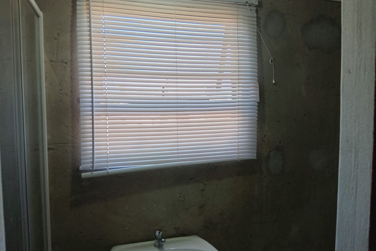 A bathroom space featuring a pedestal basin and shower enclosure, currently requiring wall finishing and cosmetic attention.