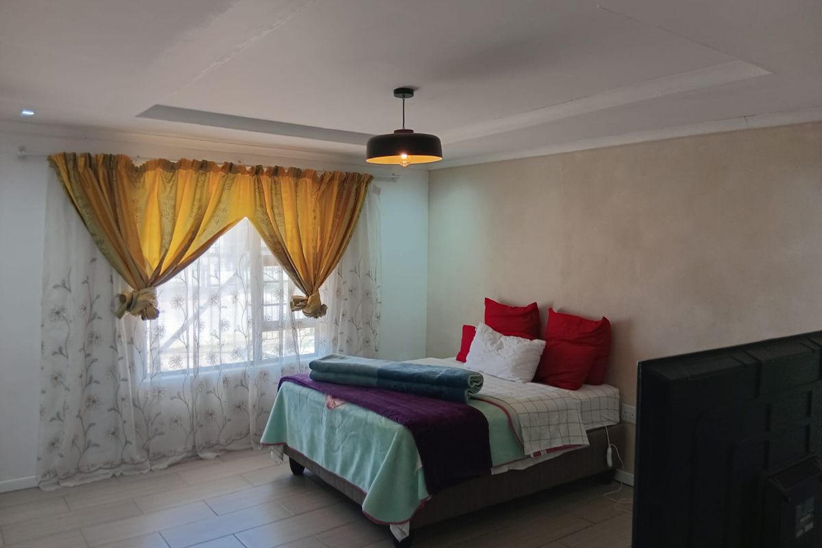 A bedroom featuring tiled flooring, a recessed ceiling detail, and a central pendant light fixture.