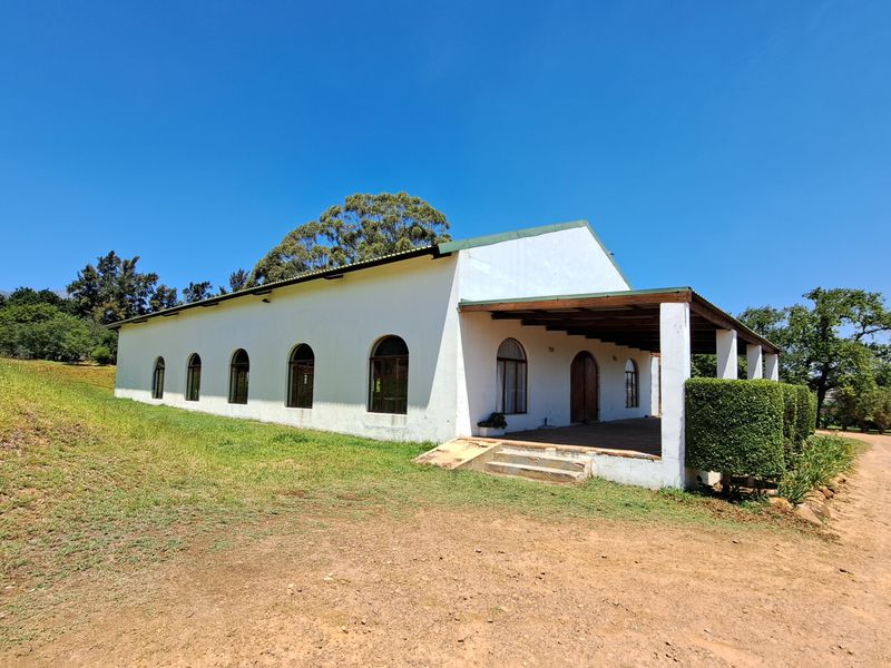 Rear view of a white farmhouse featuring a covered patio, arched windows, and a timber roof structure set on a rural property.