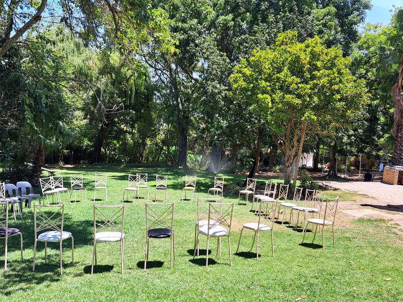 A spacious, well-maintained garden featuring mature trees, lush lawn, brick paving, and a built-in outdoor braai area.