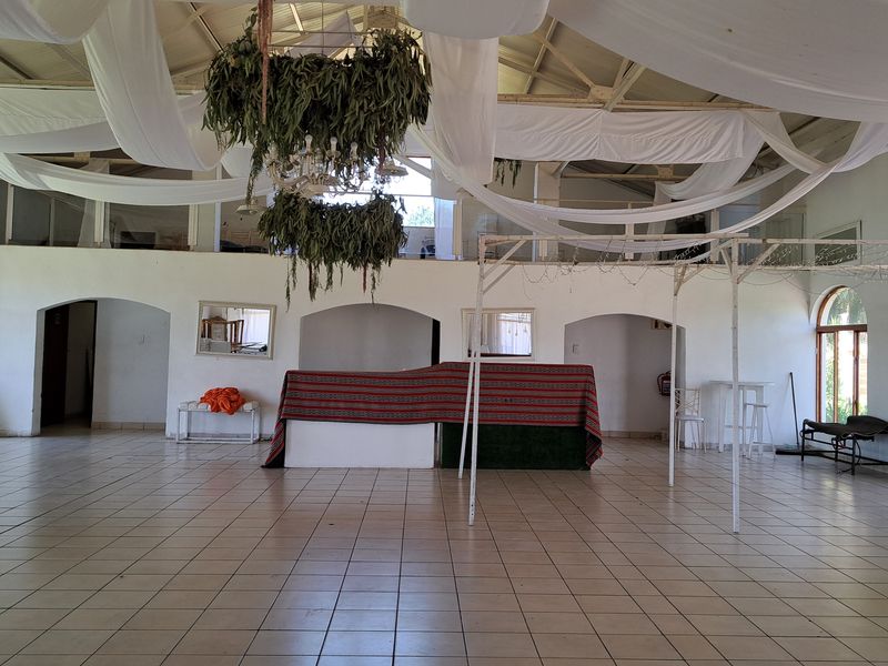 Spacious event hall featuring high ceilings with exposed steel trusses, tiled flooring, arched architectural details, and a built-in fireplace, suitable for various functions.