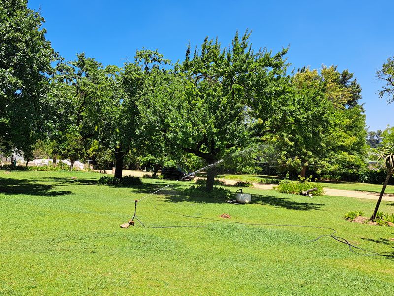 A spacious, well-maintained garden area featuring mature trees, expansive lawn, and an active irrigation system.