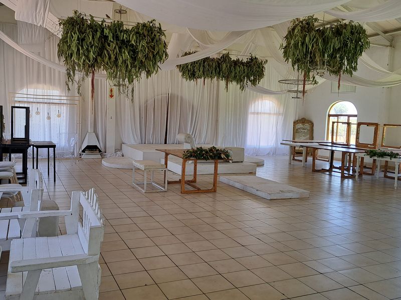 Spacious event hall featuring tiled flooring, a vaulted ceiling with draped fabric, a built-in fireplace, and a raised stage area with arched windows.