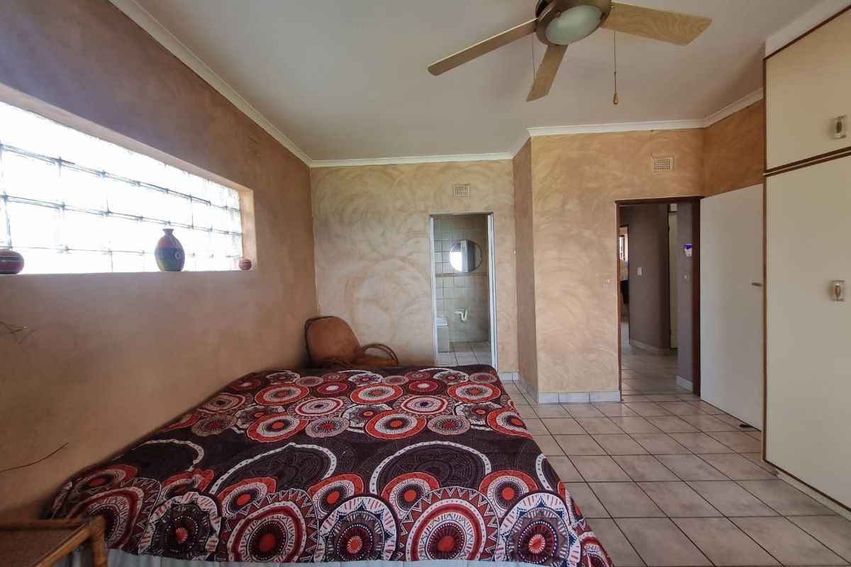 Spacious bedroom featuring tiled flooring, built-in cupboards, a ceiling fan, and a unique glass block window, with an adjoining en-suite bathroom.