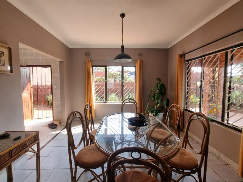 A bright dining room featuring tiled flooring, a central pendant light, and large windows with security bars, offering a view to the exterior.