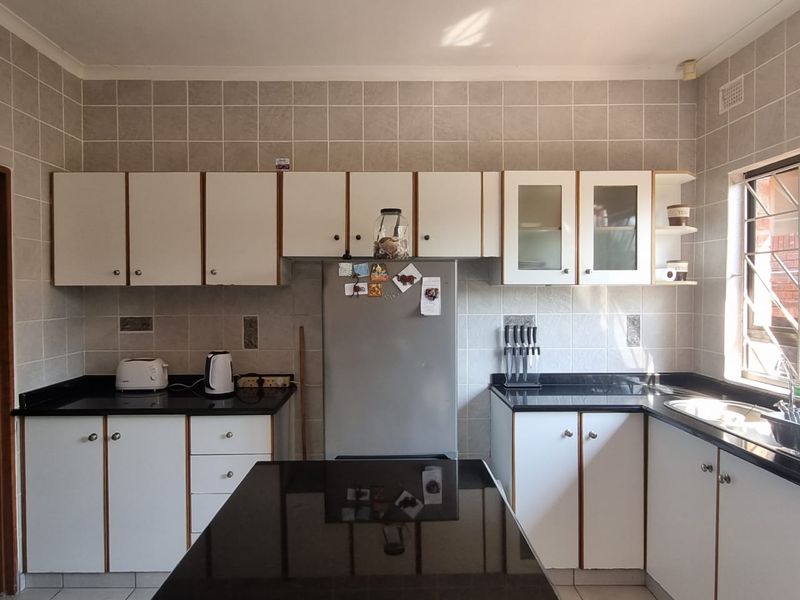 A functional kitchen featuring white cabinetry, black granite countertops, full-height tiled walls, and a stainless steel sink with natural light.