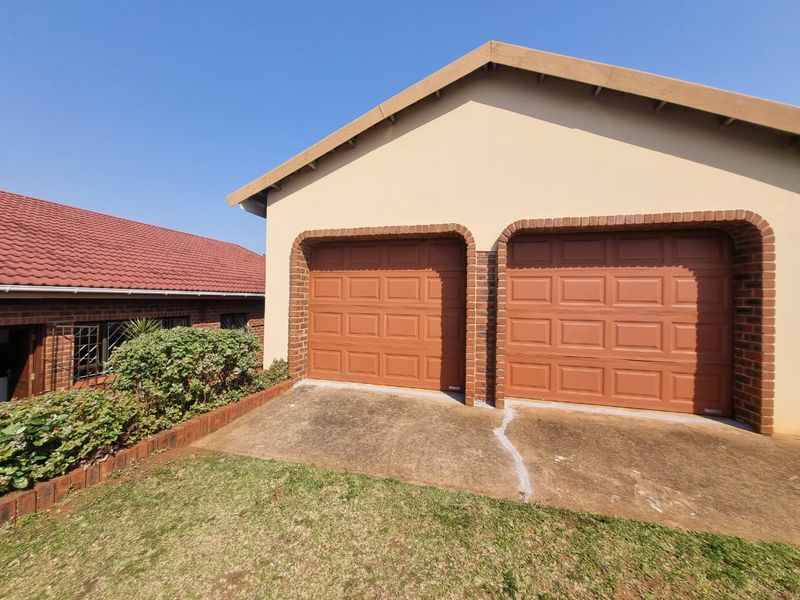 A double garage with brown sectional doors, brick trim, and a concrete driveway, situated next to a residential building with a tiled roof.
