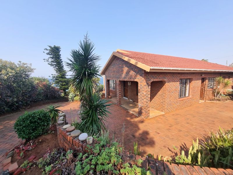 A well-maintained face brick house featuring a tiled roof, paved driveway, and a covered entrance porch, set within a landscaped garden.