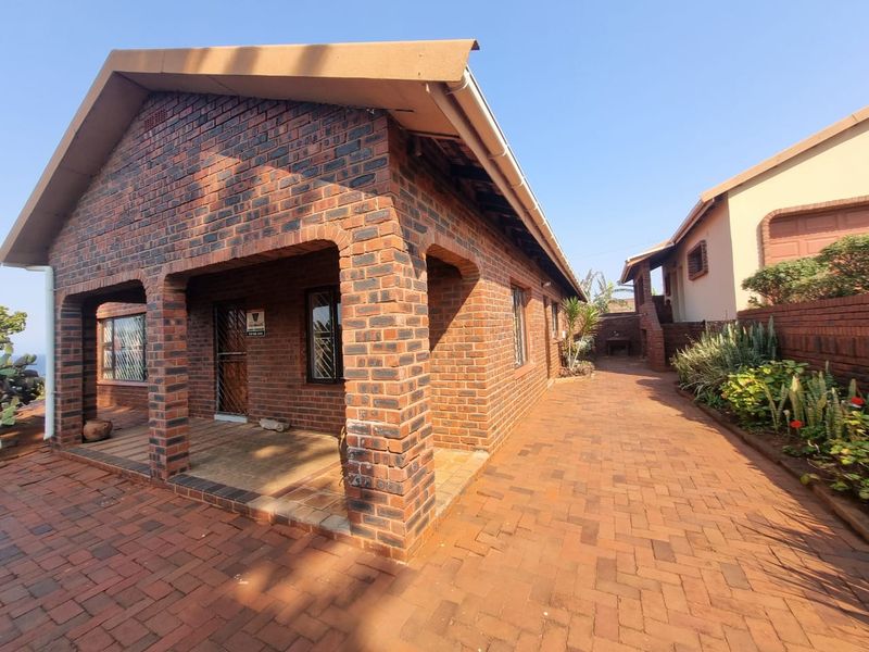 A well-maintained face brick house featuring a covered patio entrance and extensive brick paving, showcasing a classic and durable exterior design.