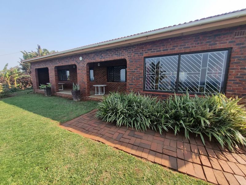 A well-maintained face brick rear exterior featuring a covered patio, paved walkway, and established garden landscaping.