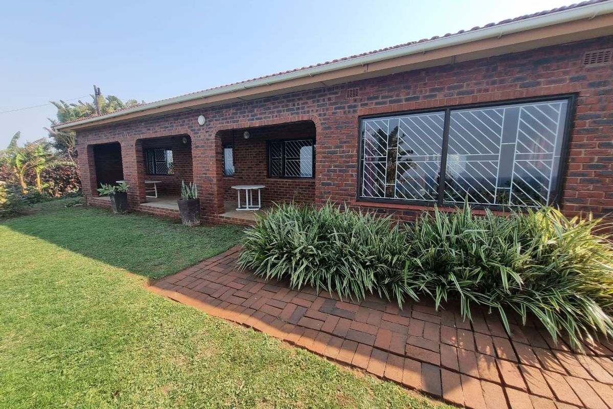 A well-maintained face brick rear exterior featuring a covered patio, paved walkway, and established garden landscaping.