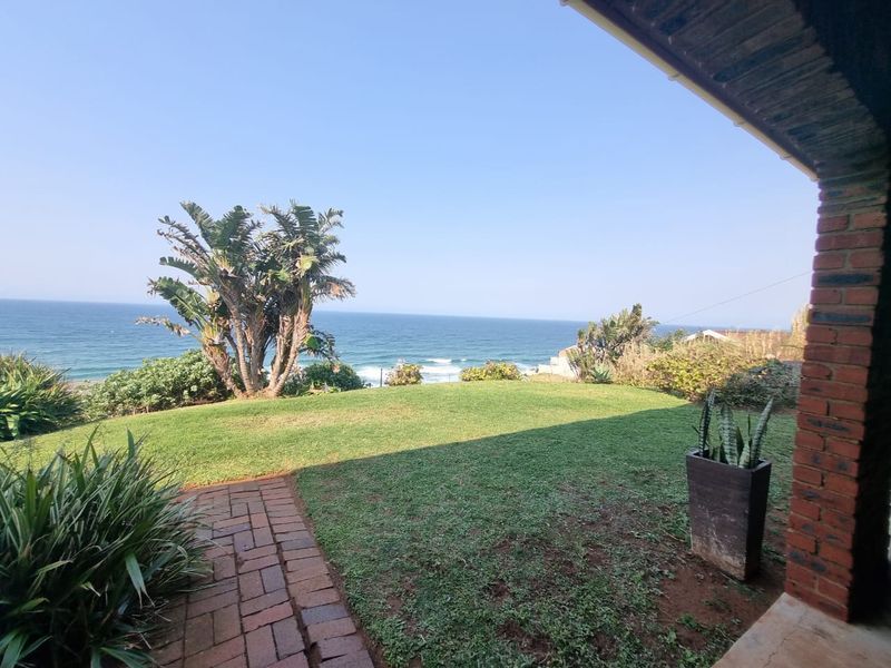 A covered patio area featuring brick paving and an exposed brick pillar, overlooking a well-maintained lawn with expansive ocean views.
