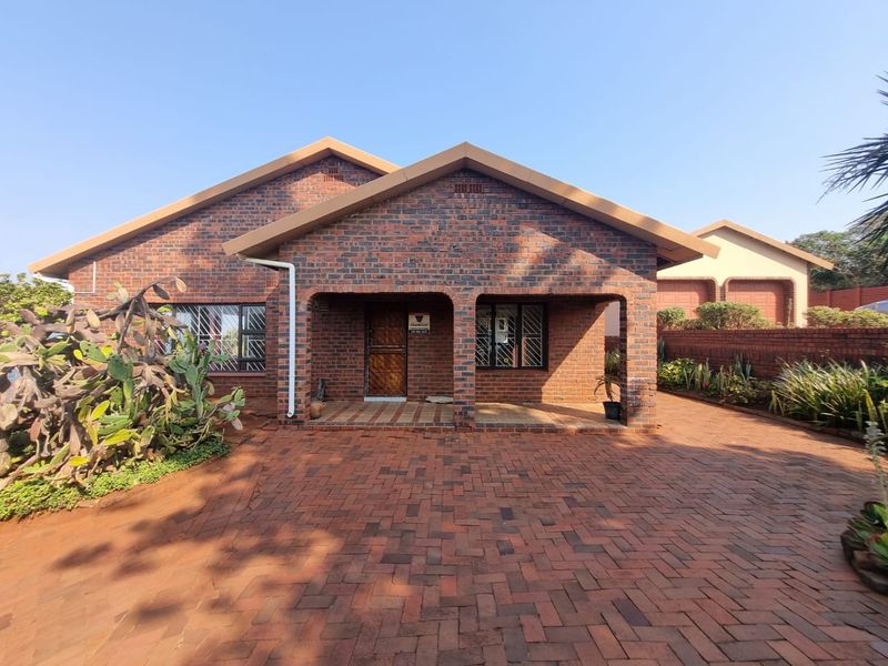 A well-maintained face brick house featuring a paved driveway, covered entrance porch, and secure window treatments.