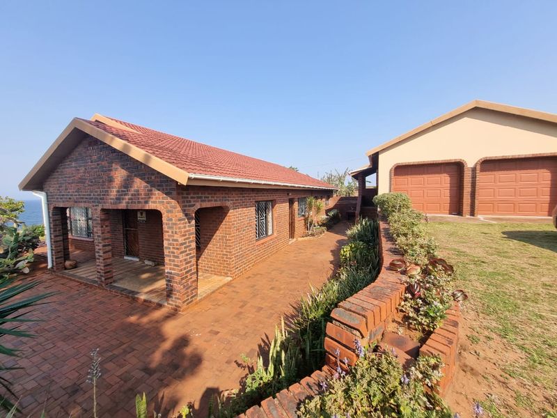 Rear view of a face brick house featuring a paved patio area, landscaped brick retaining wall, and a separate double garage.