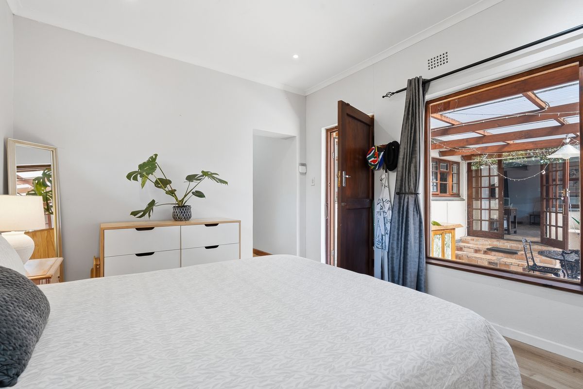 A bright bedroom featuring timber-framed windows and a door providing direct access to an outdoor patio area.