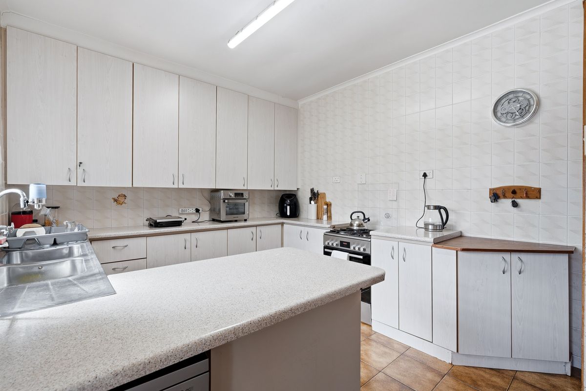Functional kitchen featuring light-toned cabinetry, stone-look laminate countertops, tiled splashbacks, and a built-in gas stove with oven.