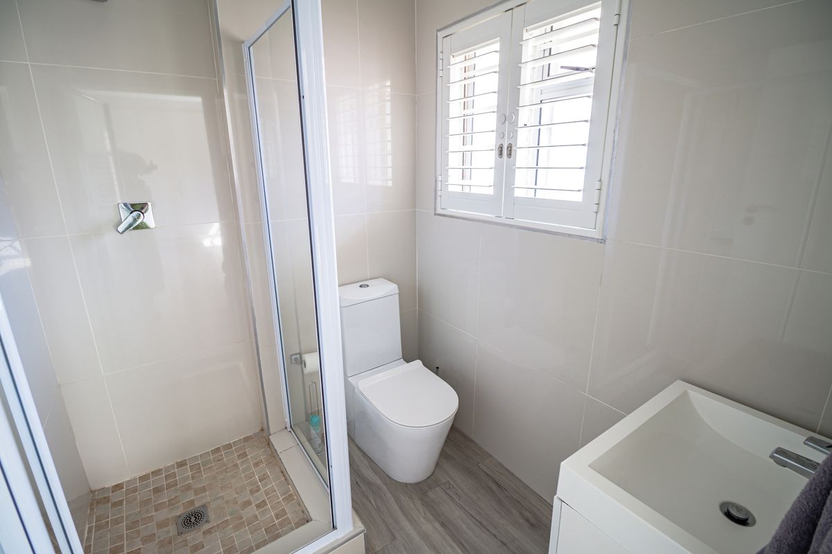 A modern, well-maintained bathroom featuring a glass-enclosed shower, a contemporary toilet, a vanity basin, and plantation-style shutters for privacy.