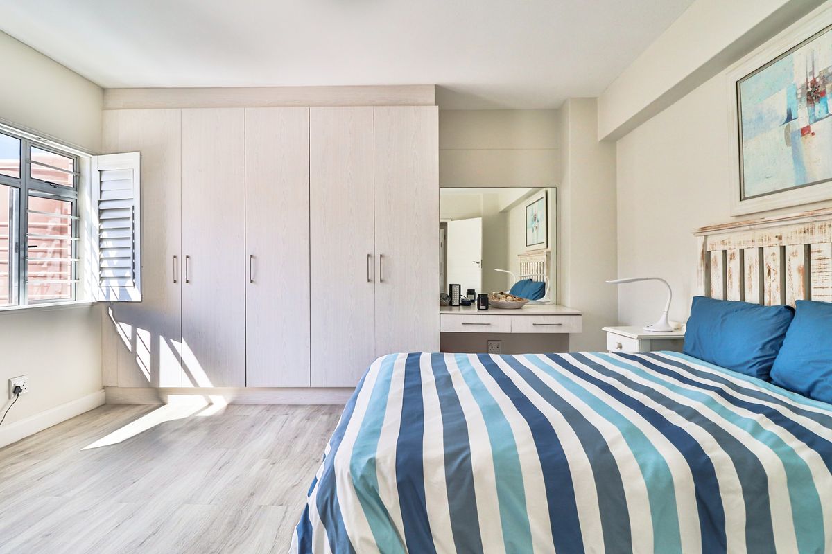 A bright bedroom featuring built-in light wood-grain wardrobes, a matching integrated vanity area, and modern wood-look laminate flooring.