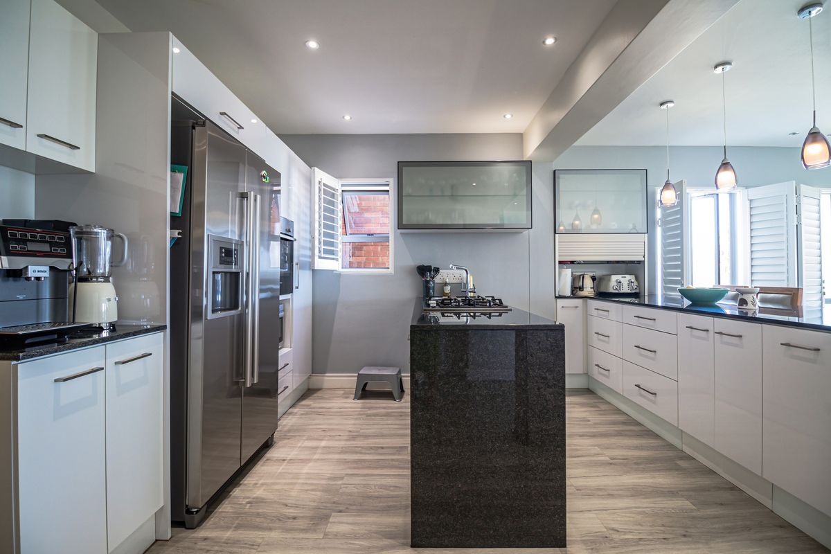 Modern kitchen featuring sleek white cabinetry, a central island with a dark granite countertop, integrated appliances, and recessed ceiling lighting.