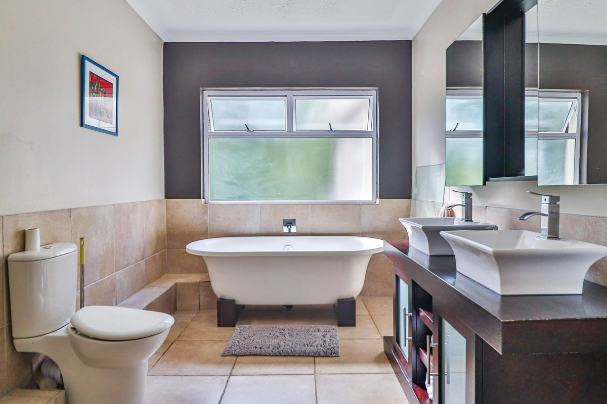 A well-appointed bathroom featuring a freestanding bathtub, dual vessel sinks on a dark wood vanity, and neutral floor-to-wall tiling.