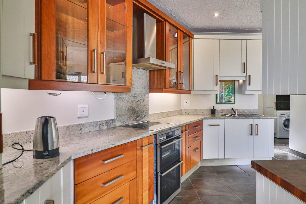 A functional kitchen featuring a mix of wood and white cabinetry, granite countertops, built-in oven, extractor fan, and a stainless steel sink.