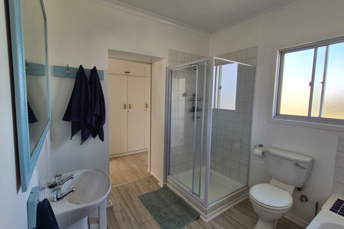 A functional bathroom featuring a pedestal basin, glass-enclosed shower, toilet, and built-in storage cupboards with light wood-look flooring.