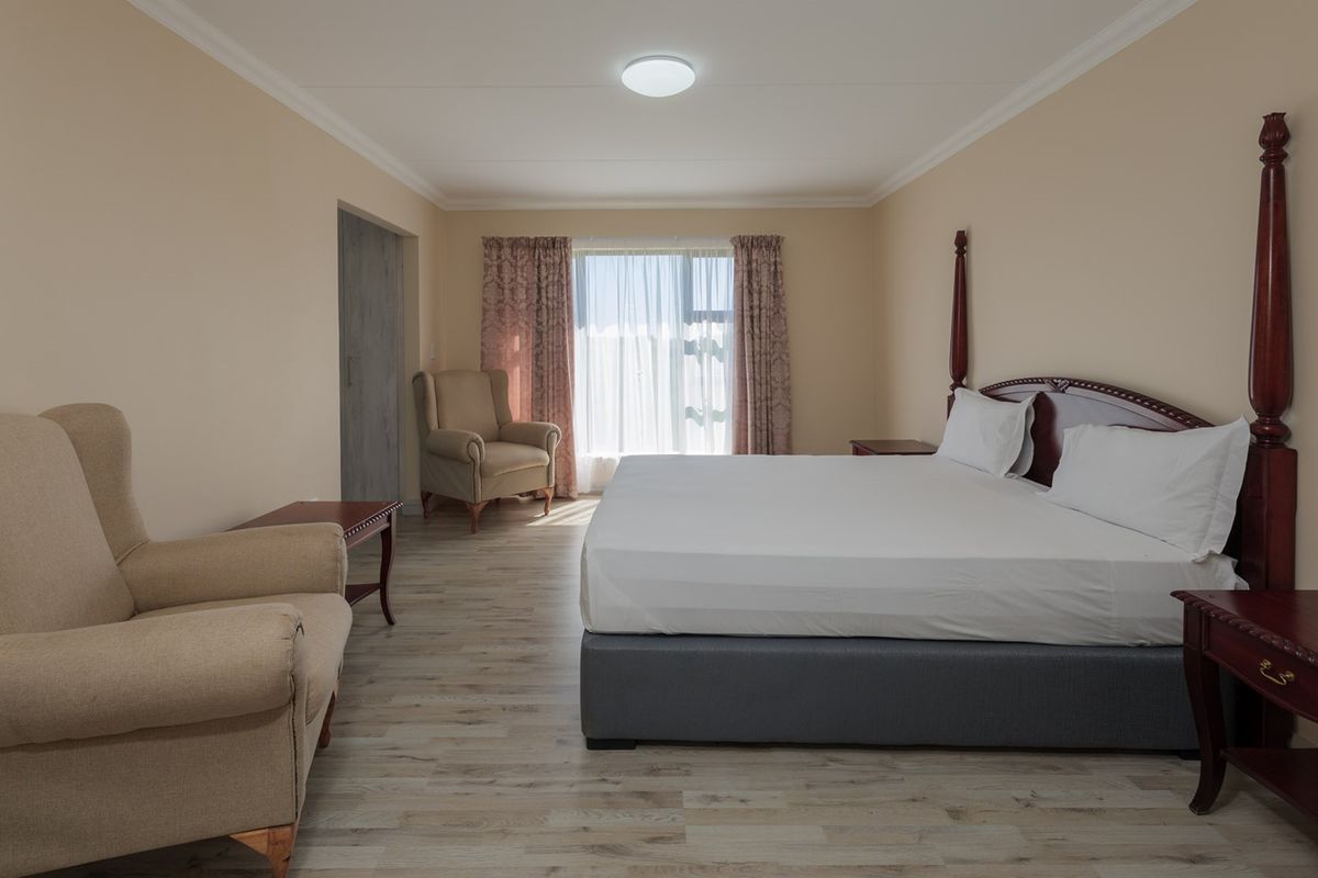 Spacious bedroom featuring light-toned laminate flooring, neutral wall finishes, and a large window with integrated curtain tracks.
