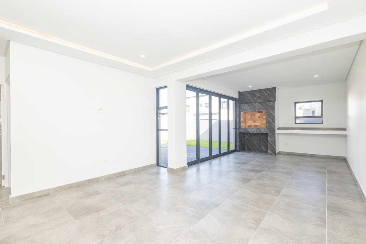 Spacious open-plan living area featuring modern grey floor tiles, recessed ceiling lighting, a built-in fireplace, and large aluminium sliding doors leading to the garden.