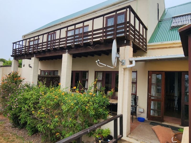 Rear elevation of the house featuring a timber balcony, corrugated metal roof with solar water heater, and multiple timber-framed access doors.