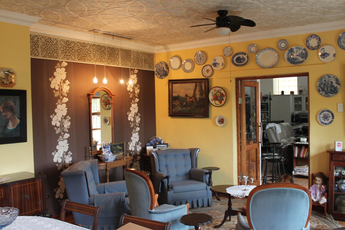 A living room featuring a decorative pressed metal ceiling, ceiling fan, and ornate wall fretwork, providing a traditional aesthetic with a view into the adjacent room.