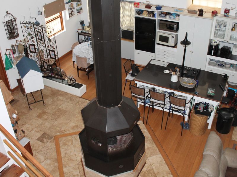 Spacious open-plan living and kitchen area featuring a central freestanding fireplace, stone flooring, and extensive built-in cabinetry with integrated appliances.